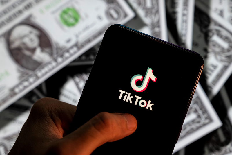  En esta ilustración fotográfica, se muestra un logotipo de TikTok en un teléfono inteligente con la moneda USD (dólar estadounidense) en el fondo.