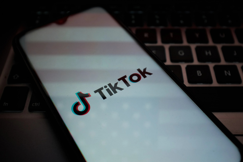  El logotipo de TikTok aparece en la pantalla de un teléfono con una bandera estadounidense reflejada en él.