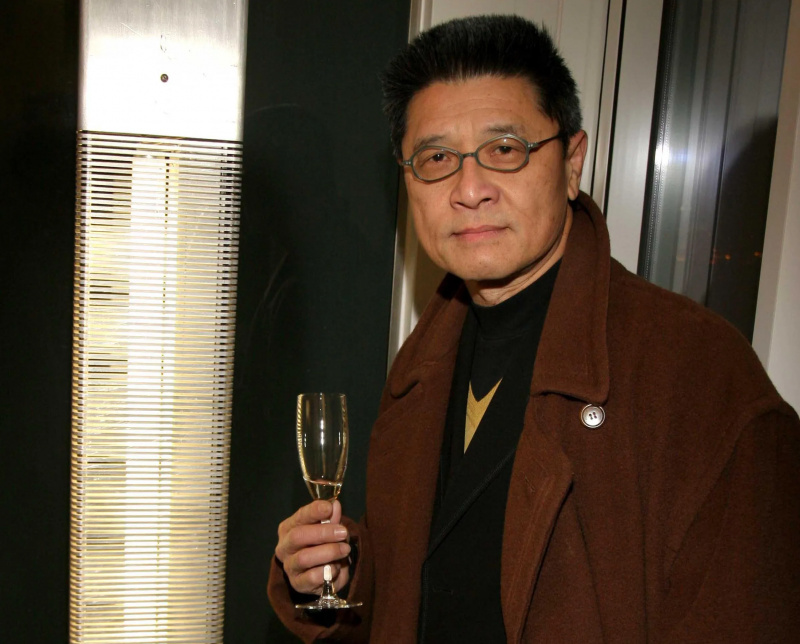  Bărbat de vârstă mijlocie de origine asiatică americană care poartă ochelari și haină maro ține un pahar de șampanie