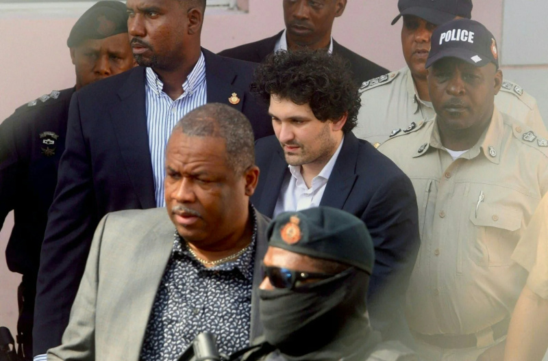  Sam Bankman-Fried îmbrăcat în costum, escortat de autoritățile din Bahamas